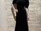 a woman standing in front of a brick wall wearing a black dress