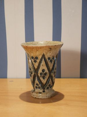 un petit vase posé sur une table, avec un mur rayé en arrière-plan