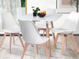 une table blanche avec quatre chaises et un bol de fruits posé dessus