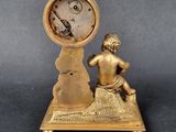 brass figurine of a boy sitting on a rock with a clock in the background