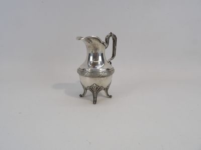 un petit pichet en argent posé sur un socle, sur une surface blanche