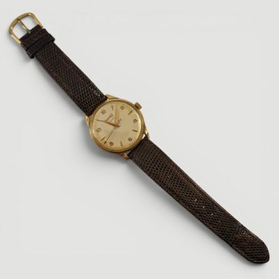 gros plan d'une montre sur une surface blanche avec un bracelet marron
