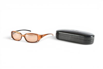 une paire de lunettes de soleil marron et un étui noir posés sur une surface blanche