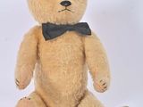 un ours en peluche marron avec un nœud papillon, assis sur une surface blanche