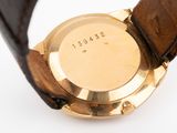the back of a watch with a gold case and brown leather band