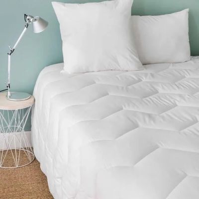 un lit recouvert d'une couette blanche et une table de chevet avec une lampe