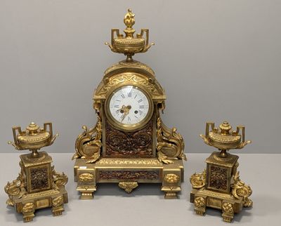 une horloge en or et trois bougies posées sur une table