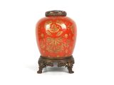 un vase rouge orné de motifs dorés, posé sur un socle