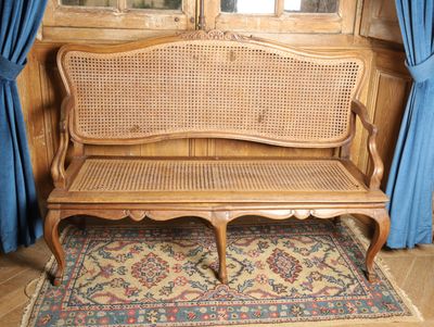un banc en bois avec un dossier en osier et un tapis posé à même le sol