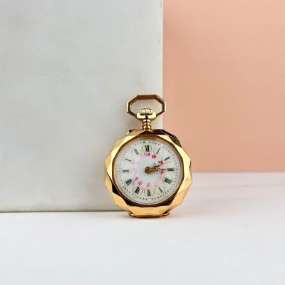 montre de poche en or avec des chiffres romains, posée sur un socle en marbre