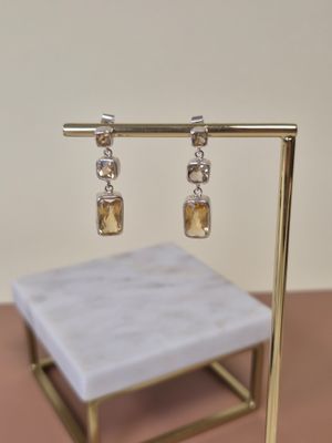 boucles d'oreilles en argent et citrine, posées sur un support en or, sur un fond rose
