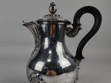 une cafetière en argent avec une poignée noire, posée sur un socle