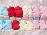 many pairs of baby mittens on a white blanket