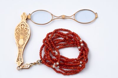 un collier de perles rouges et une paire de lunettes posés sur une surface blanche