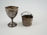 une coupe en argent à côté d'une autre coupe en argent, posées sur une surface blanche