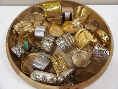 a wooden bowl filled with lots of gold and silver jewelry
