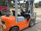 an orange forklift truck parked in a parking lot next to a red tractor