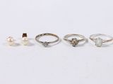 five different rings and a pearl on a white surface