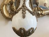 a white and gold vase sitting on a table with a mirror in the background