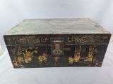 une vieille boîte noire ornée de motifs dorés, posée sur une surface blanche
