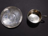 an antique silver cup and saucer on a black surface