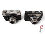 two cameras sitting next to each other on a white surface