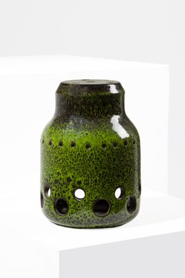 un vase vert percé de trous, posé sur une étagère blanche