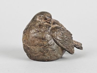 an old silver figurine of a bird sitting on top of a rock