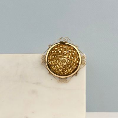 broche plaquée or posée sur un socle en marbre, sur fond bleu