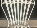 a white metal chair that is sitting on the sidewalk