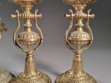 three antique brass candlesticks on a table with a clock in the background