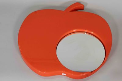 un miroir orange en forme de pomme posé sur une surface blanche