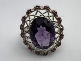 a close up of a ring with a purple stone surrounded by red stones