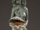 a statue of a mermaid sitting on a rock holding a shell