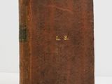 a brown book with gold lettering sitting on a white surface