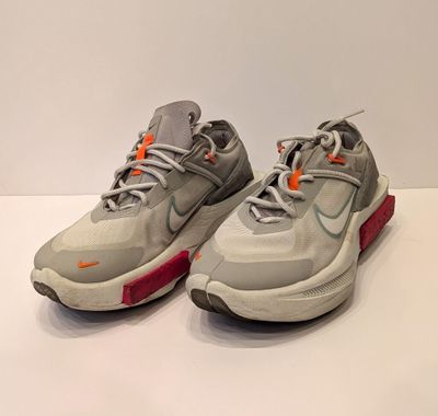 une paire de baskets grises et orange posées sur une surface blanche