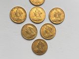 six gold sovereigns are arranged in a triangle on a white surface