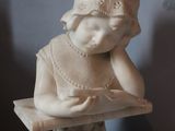 a marble statue of a girl reading a book on a table