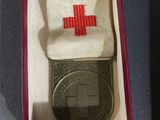 a red cross medal in a box with a keychain