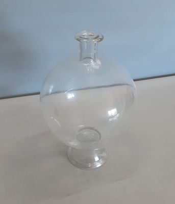 un vase en verre transparent posé sur une table, avec un mur bleu en arrière-plan