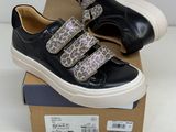 des baskets noires et blanches ornées de lanières à imprimé léopard, posées sur une boîte en carton