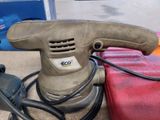 a sander that is sitting on the ground next to a red bag