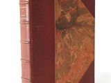 an old book with a red cover sitting on top of a white surface