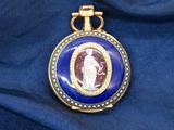 une image représentant une montre de poche bleue et dorée sur laquelle figure le portrait d'une femme