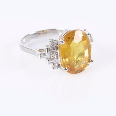 a close up of a yellow sapphire and diamond ring on a white surface