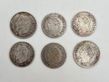 six types différents de pièces d'argent posées sur une surface blanche