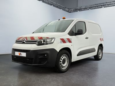 La camionnette blanche est garée dans une grande pièce ; elle porte une bande rouge sur le côté.