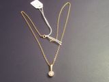 two gold necklaces with a white diamond on a black surface