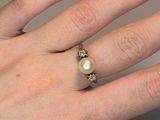woman ' s hand with a pearl and diamond ring on it ' s finger