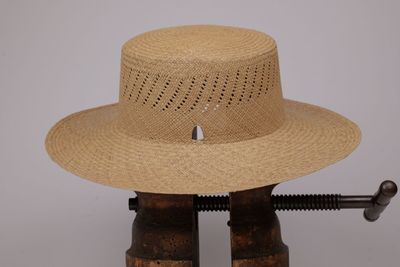 une image représentant un chapeau de paille posé sur un support en bois, à côté d'un pistolet